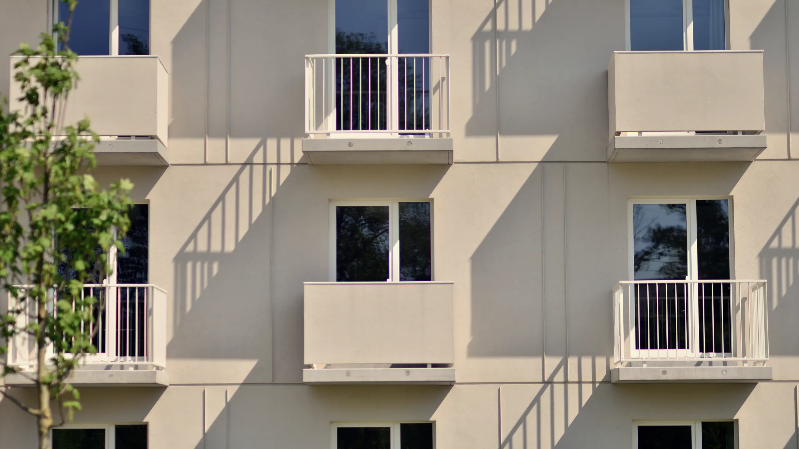 Helle Fassade eines Mehrfamilienhauses mit Balkonen im Streiflicht